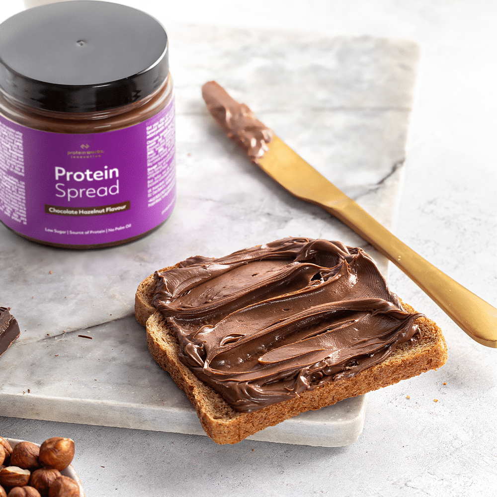 Proteincreme auf einer Scheibe Toast neben einem Messer und der Proteincreme Dose auf Marmortablet.