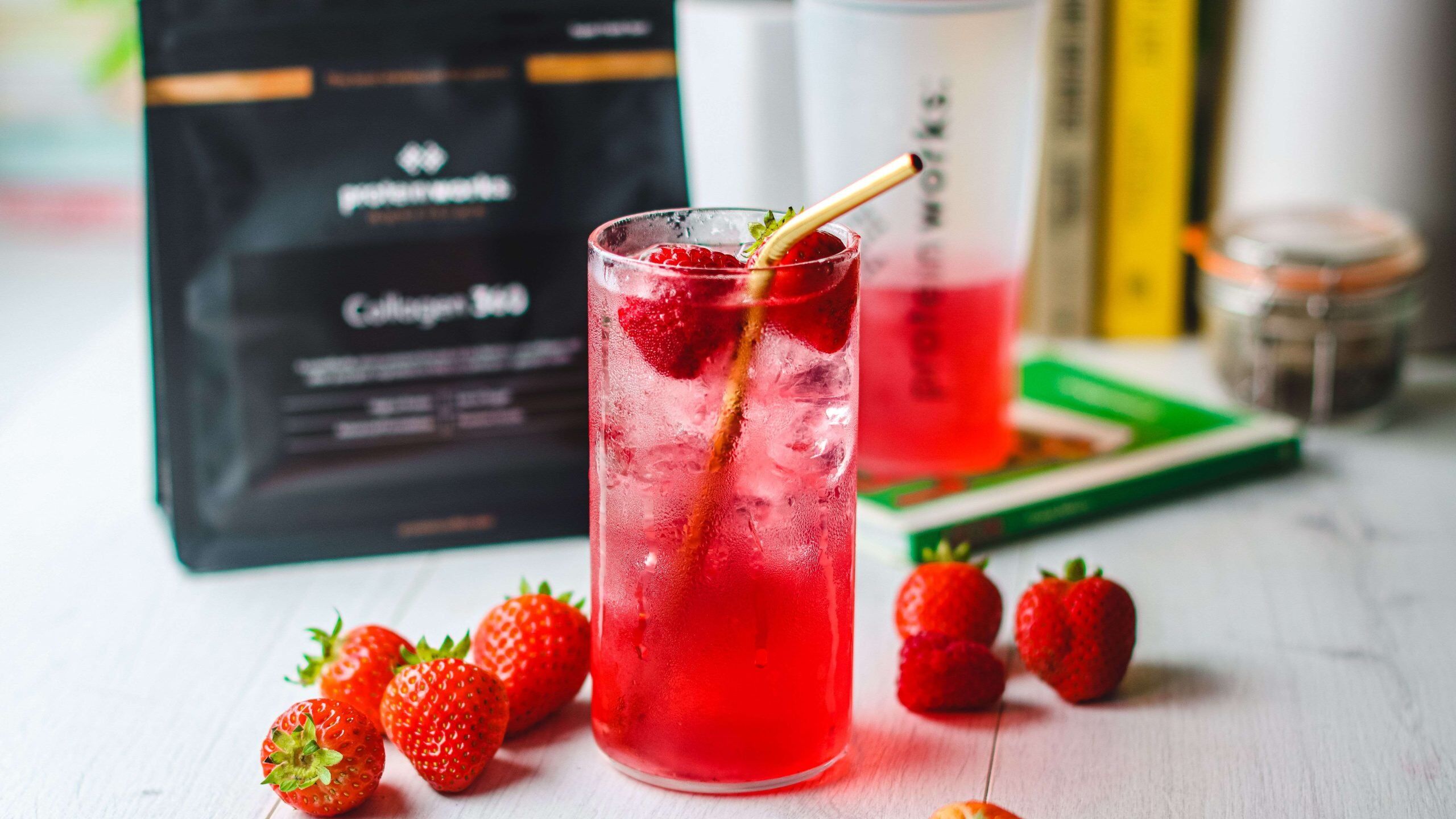 Vibrant red Clear Collagen Drink in clear glass decorated with strawberries and a gold straw